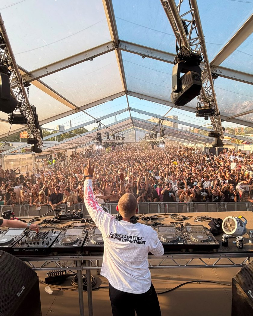 A packed festival tent at golden hour, hands in the air in front of the DJ booth.